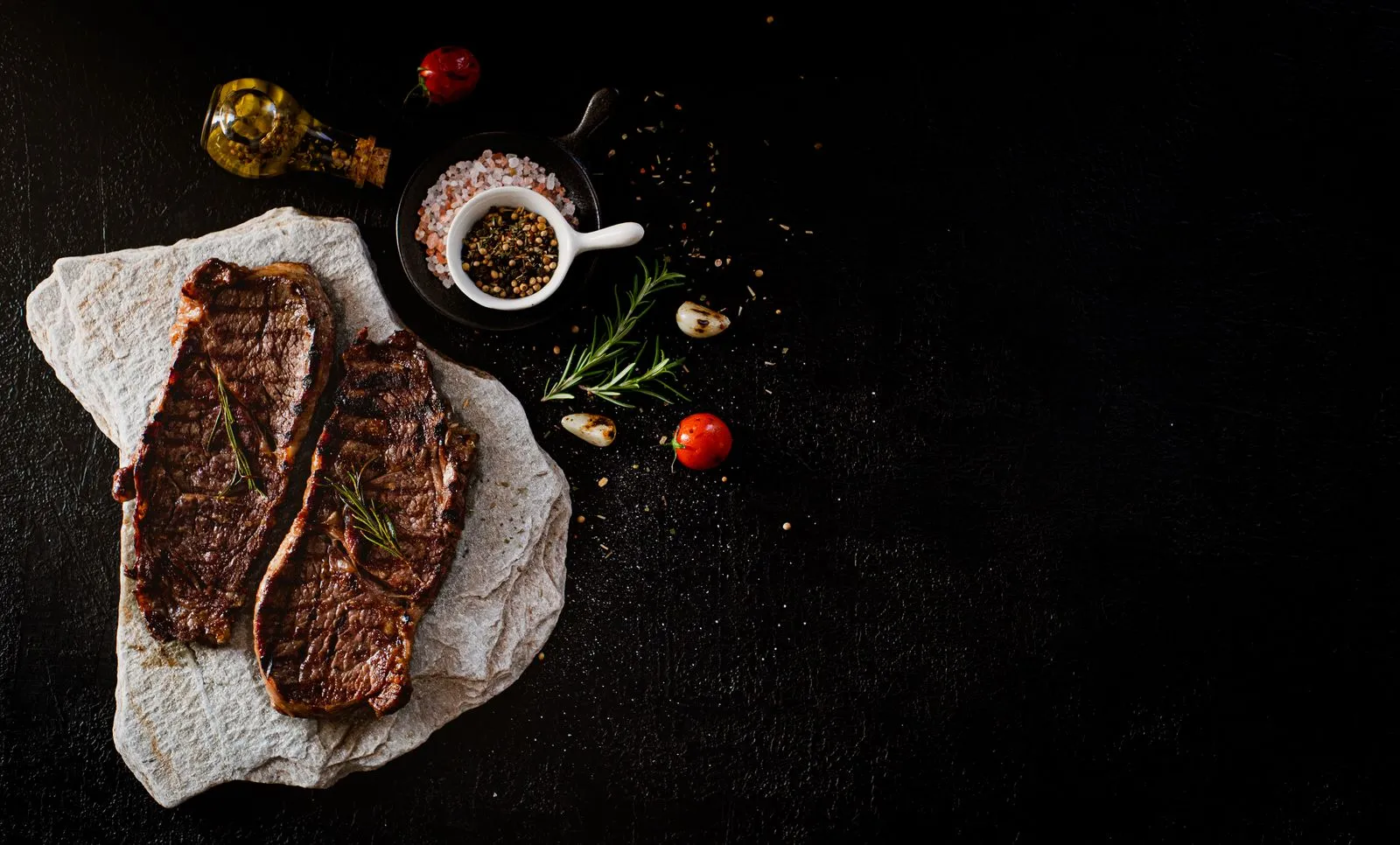 Deux steaks crus assaisonnés sur une table sombre